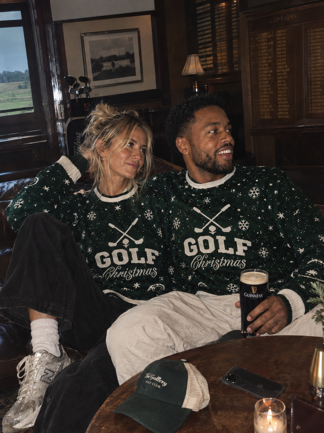 A man and a woman sitting together in a dimly lit pub wearing matching dark green Christmas sweaters with white snowflake and golf club graphics and the words 'GOLF Christmas'. The man holds a pint of Guinness.